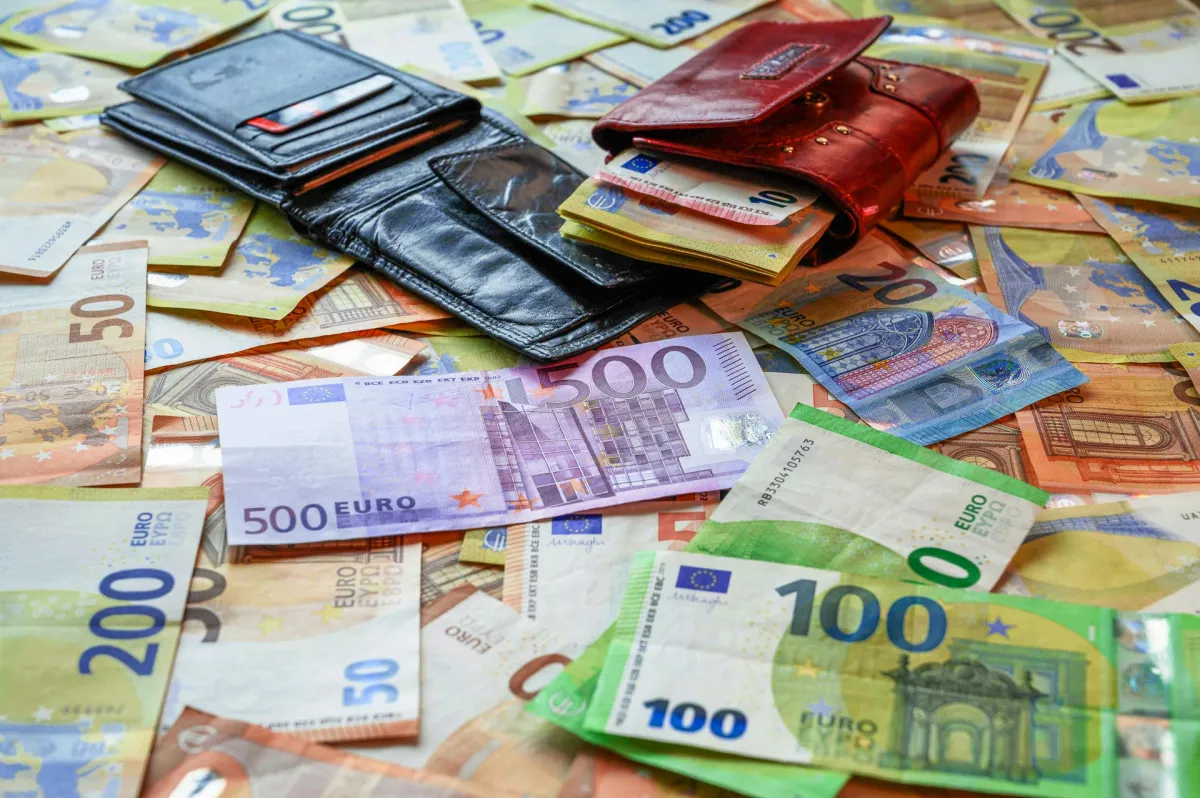 A black and a red leather wallet resting on a scattered pile of euro banknotes in various denominations.